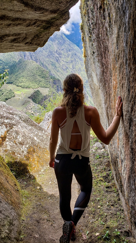       Woman looking out from rocks with a view of ancient terraces.
  