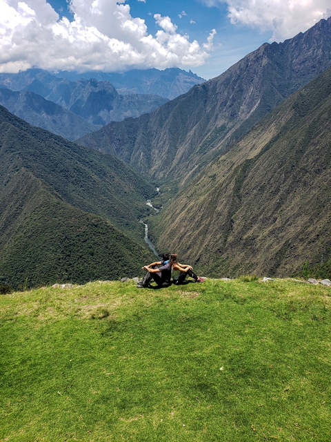      Couple sitting on grass with panoramic valley view.
  