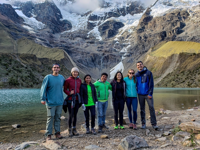       Group posing by a mountain lake with a glacier backdrop.
  