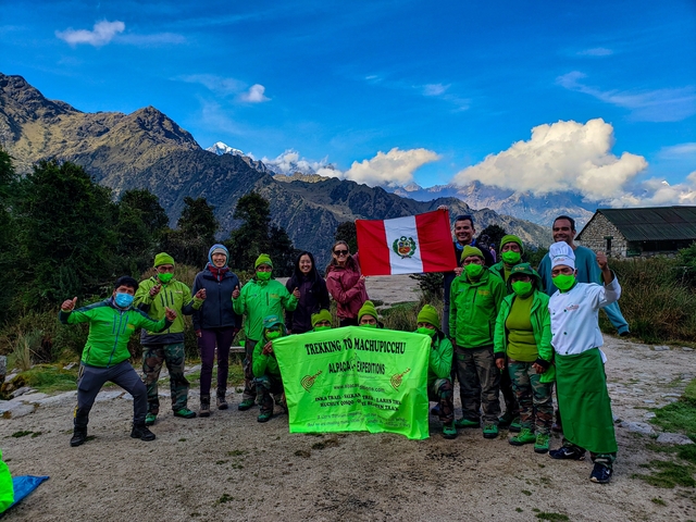       Group with flag posing for a photo with mountain scenery.
  