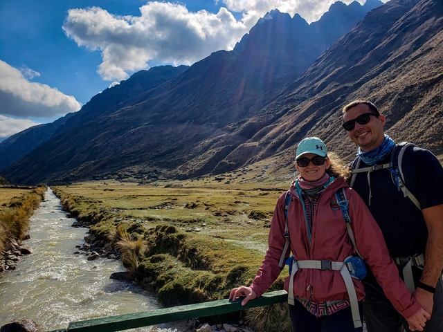       Couple posing in a valley with mountains beside a river.
  