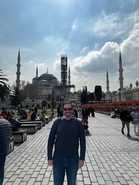 A person posing in a busy street with architectural landmarks in the background.