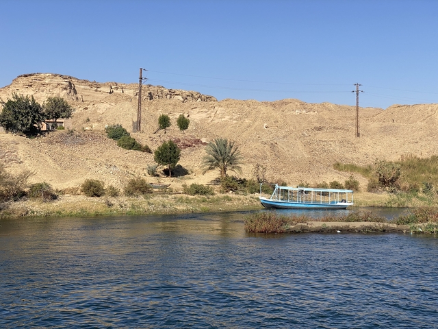       A small boat on the Nile River with arid hills.
  