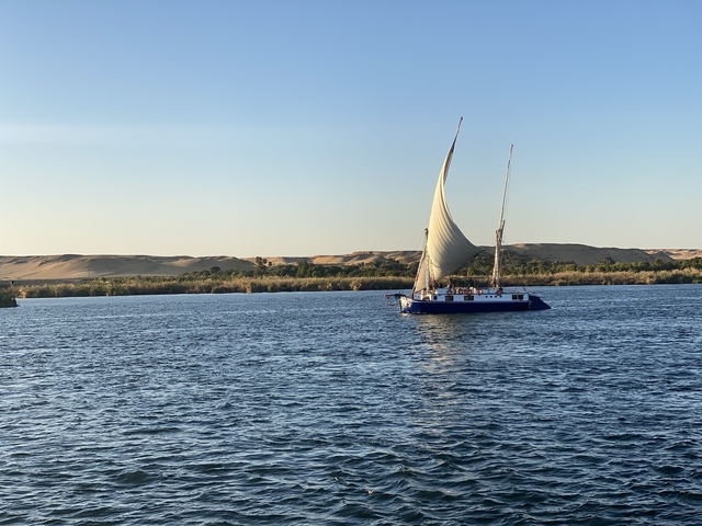       A sailboat on the Nile River with sandy dunes in the background.
  
