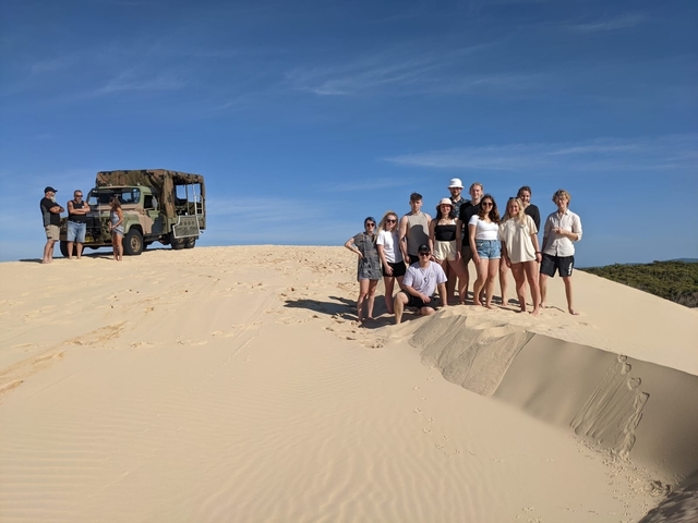 Group of people on sand dunes with an off-road vehicle.