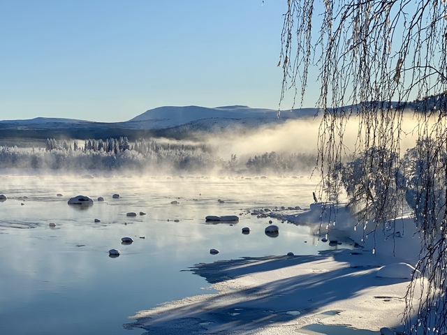Snowy landscape with mist over a frozen river.