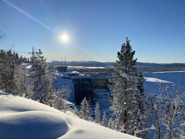 Winter landscape with an industrial structure and distant mountains.