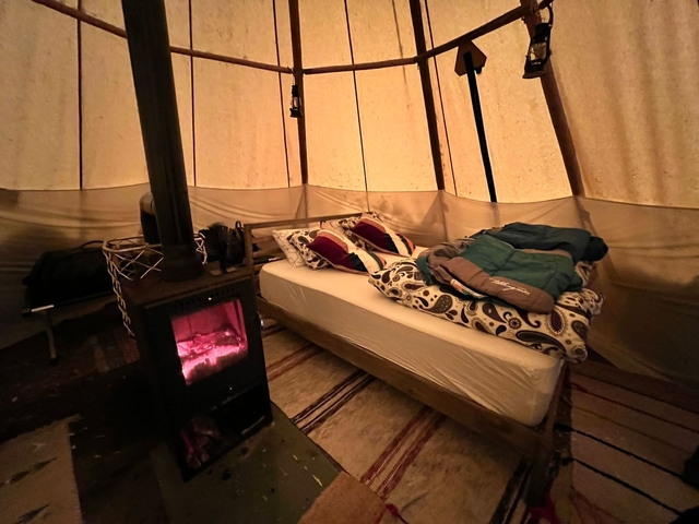       Interior of a tent with a bed and wood stove.
  