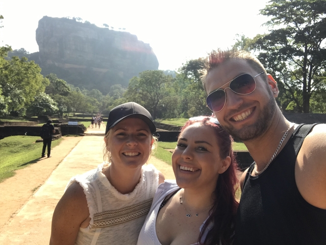 Three people taking a selfie with a large rock formation.