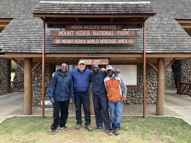       Four people posing in front of the Mount Kenya National Park entrance.
  