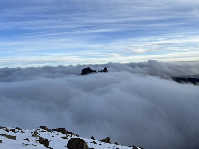       A view above the clouds with mountain peaks visible.
  