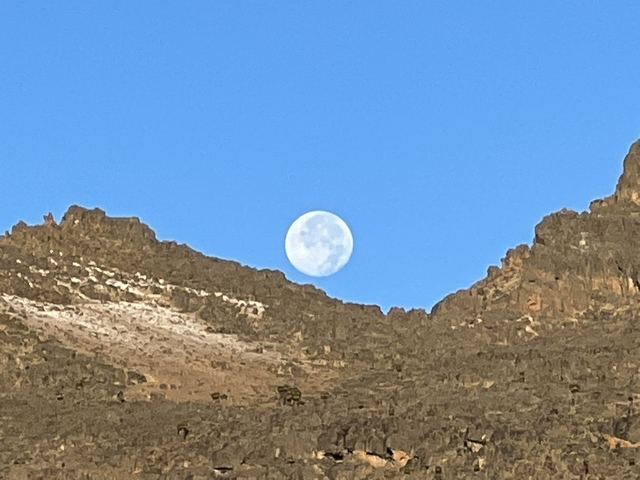       Full moon visible between rugged mountain peaks.
  