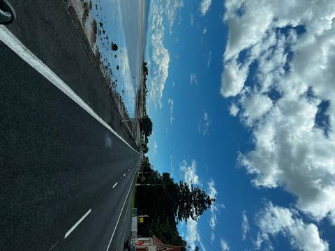 A straight road with reflections of clouds on water beside it.
