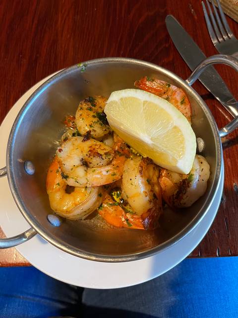A dish of grilled prawns with a lemon wedge in a metal bowl.