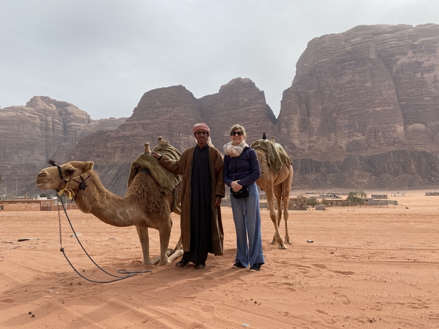 Two people with camels in the desert with rocky hills.