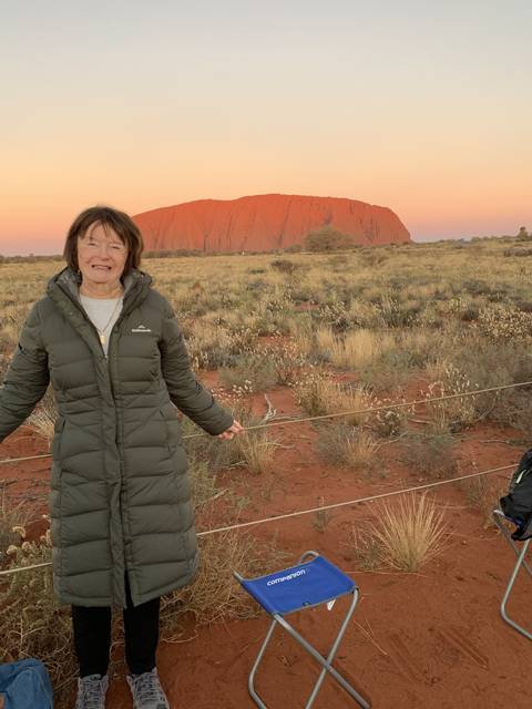       Person smiling in front of desert and mountain landscape during sunset.
  