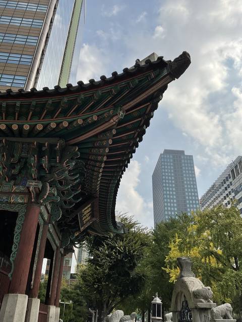       Traditional Korean roof with modern buildings in the background.
  
