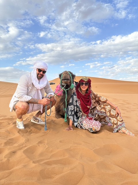 Two people posing with a camel in the desert