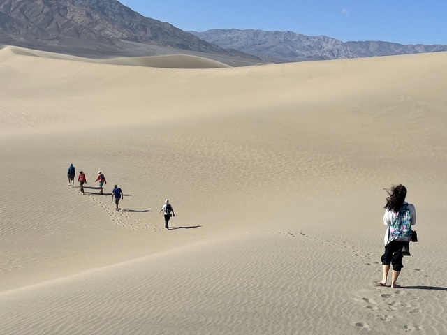       A group of people walking across sand dunes.
  