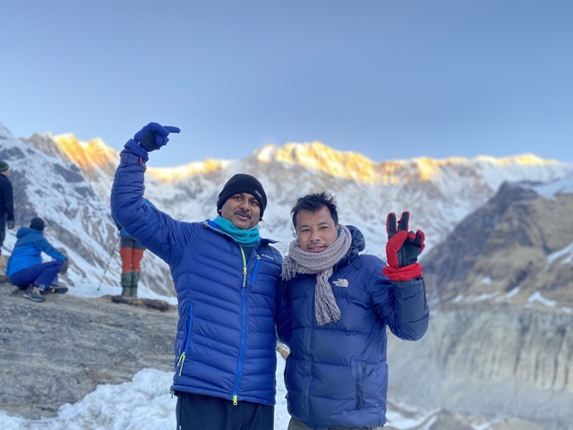 Two men in winter clothing with snowy mountains in the background.