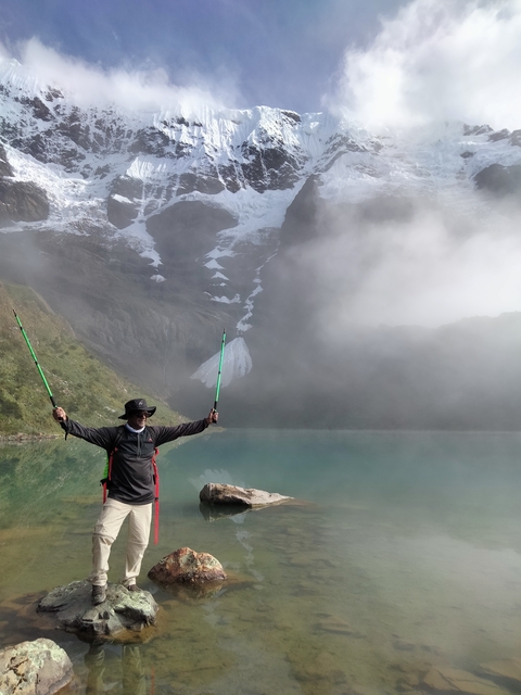 Person standing with hiking poles by a misty lake with mountains.