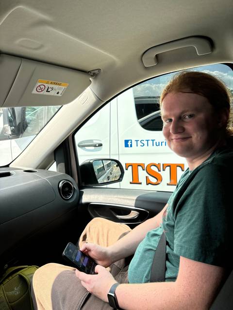 Person sitting inside a vehicle with a logo visible on the window.