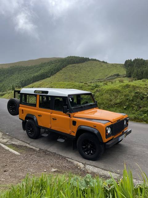 Orange vehicle parked by a mountainous road.