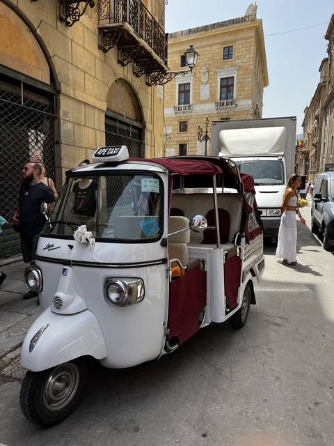       Tuk-tuk parked on a city street with vintage buildings.
  