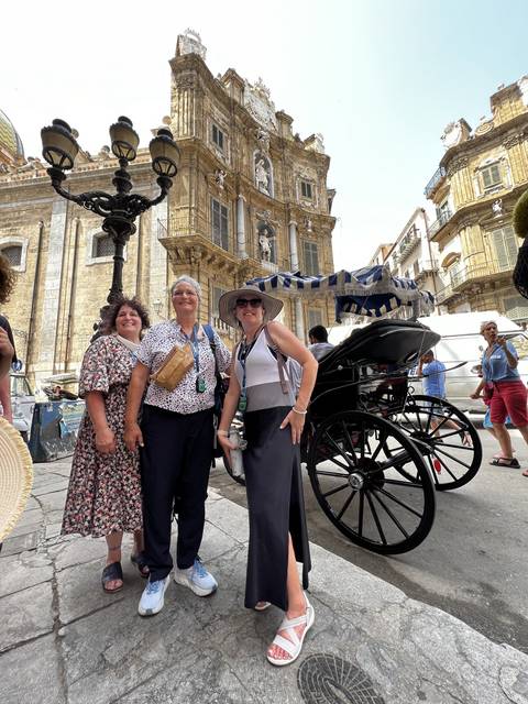       Three people standing with a cart on a city street with historical architecture.
  
