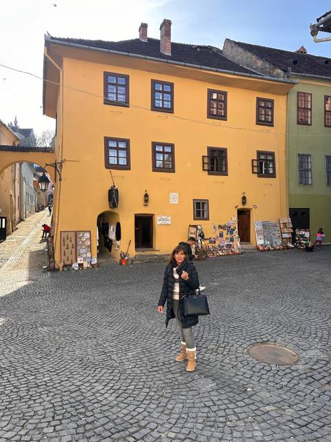       Person standing in front of a yellow building with a display of souvenirs.
  