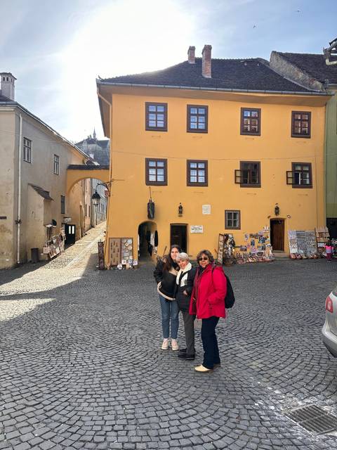       Two people posing in front of a yellow building displaying souvenirs.
  
