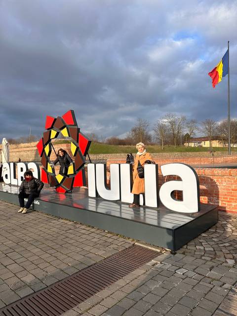       People posing in front of a sign with a modern art structure.
  