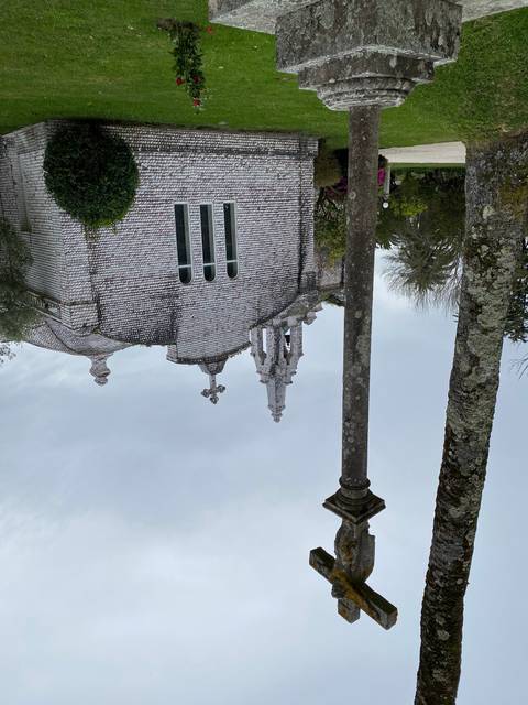 Stone building with a cross and trees in a park setting.