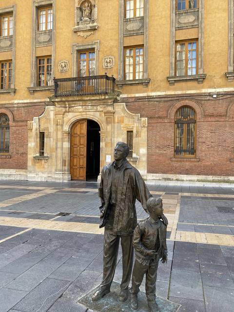 Statue of a man and a child in front of a historic building.
