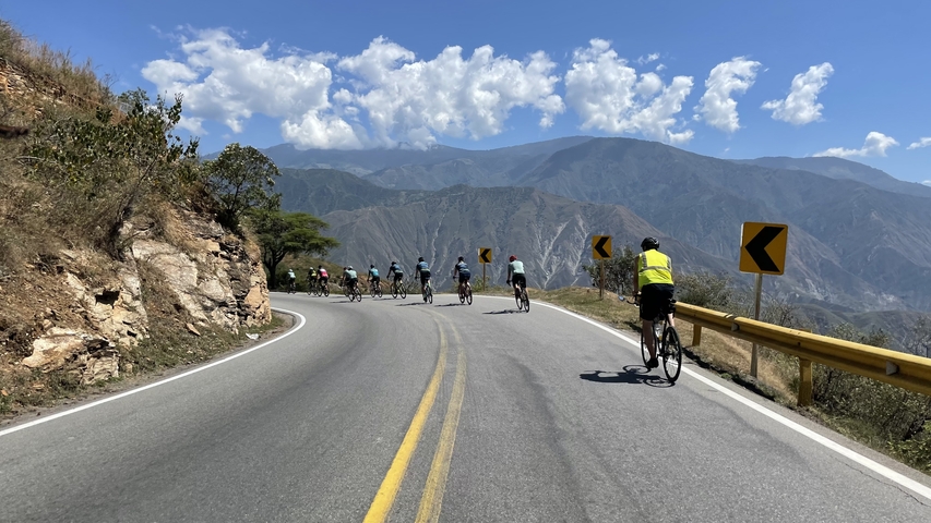       Cyclists on a winding road with mountainous scenery.
  