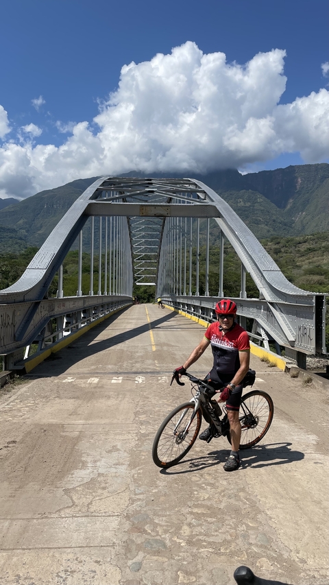       Cyclist posing on a bridge with a scenic valley in the background.
  