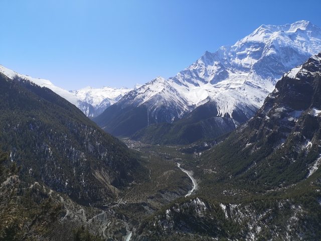 Panoramic view of a valley with a river and snow-covered mountains.