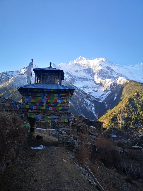 A tower with prayer flags and a backdrop of snowy mountains.