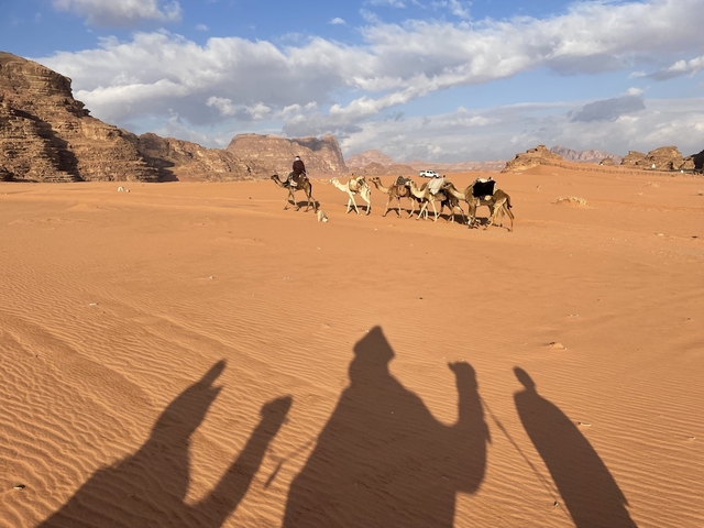 Camel caravan traversing a sandy desert with rocky formations.