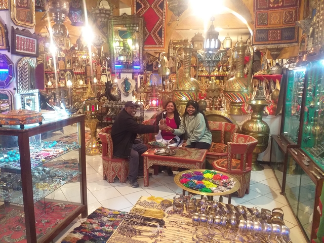Three people sitting in a shop with traditional Moroccan items.