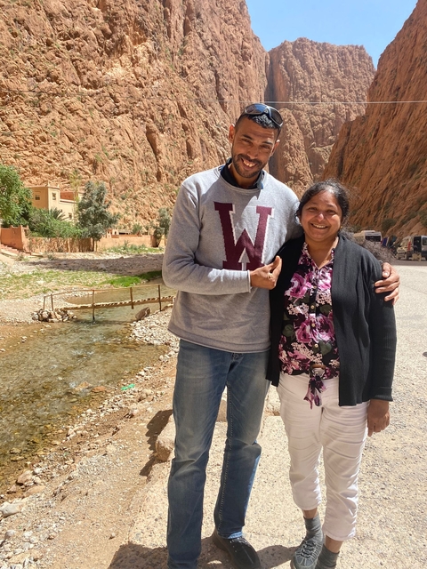 Two people posing near a small bridge and stream.