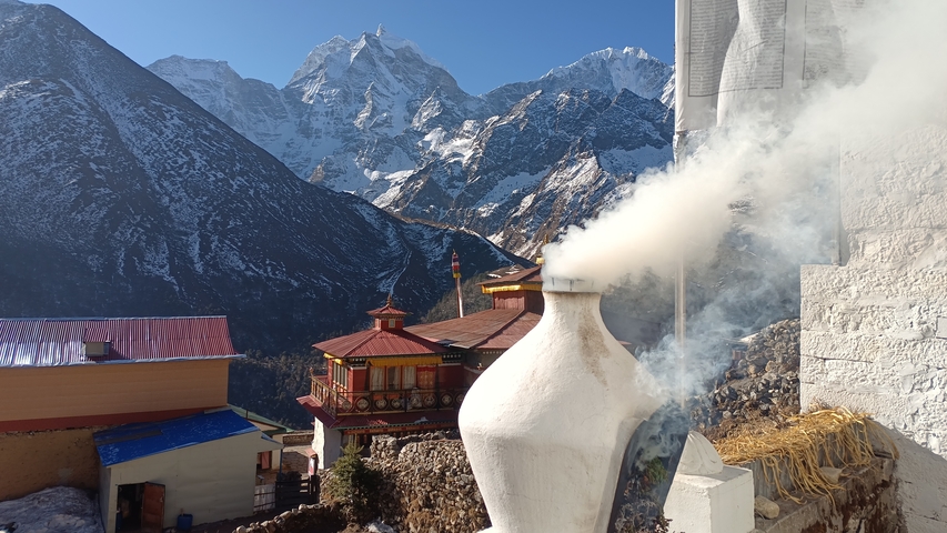 Smoke rising from a religious site against a backdrop of snow-covered mountains.