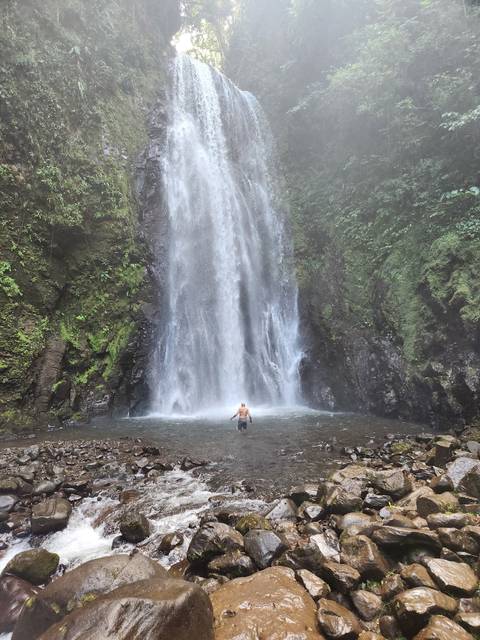       Person standing in front of a large cascading waterfall.
  