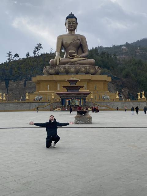 Person posing with a large Buddha statue.