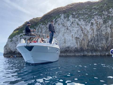       People on a boat near a rocky cliff under a blue sky.
  