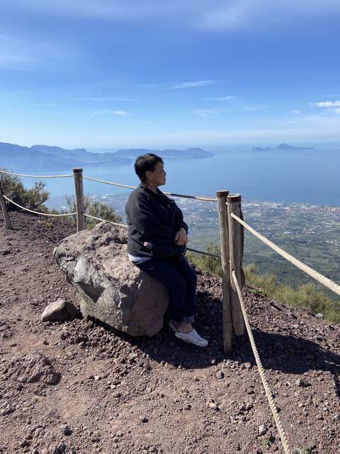       Woman sitting on a stone with a coastline view.
  
