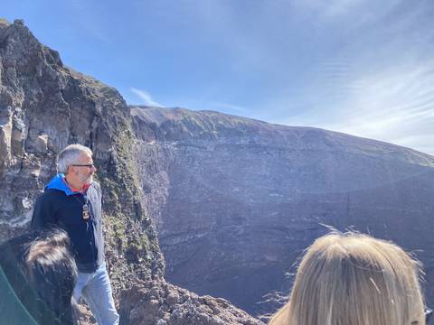       Person standing on the edge of a volcanic crater with clear blue sky.
  