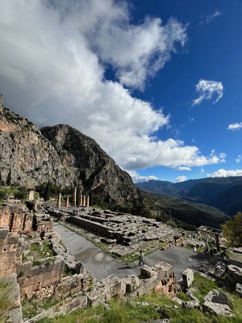       Ruins of an ancient structure up a rocky hill with cloudy sky.
  