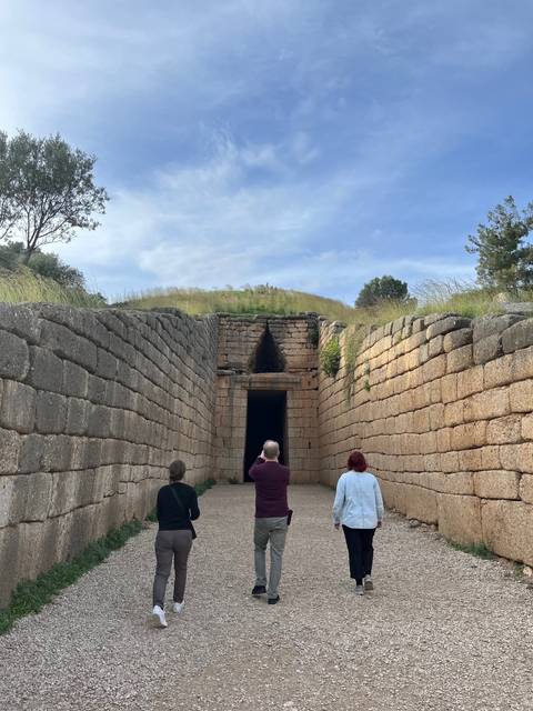       Three people walking towards an ancient tomb entrance.
  