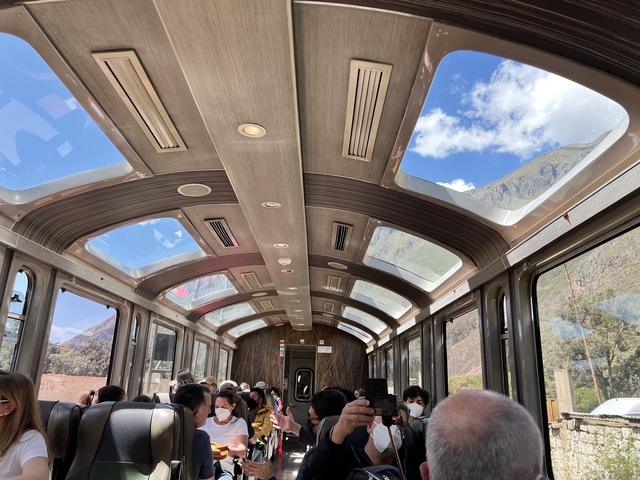 Passengers inside a train with a panoramic glass roof and mountain views.